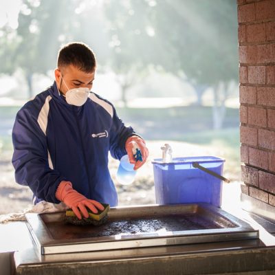 Quayclean team member disinfecting and scrubbing outdoor barbecue